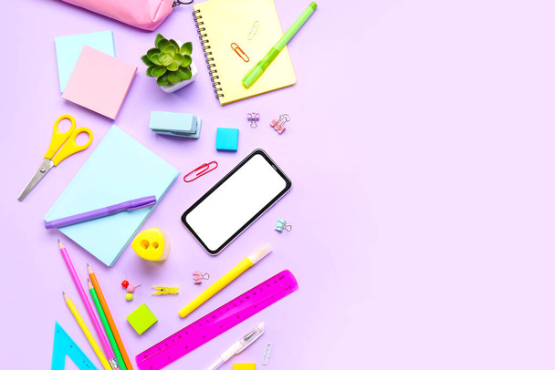 Different stationery with mobile phone on lilac background - Fotó, kép