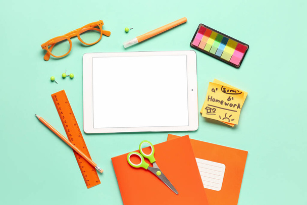 Sticky notes with word HOMEWORK, tablet and different stationery on turquoise background - Photo, Image