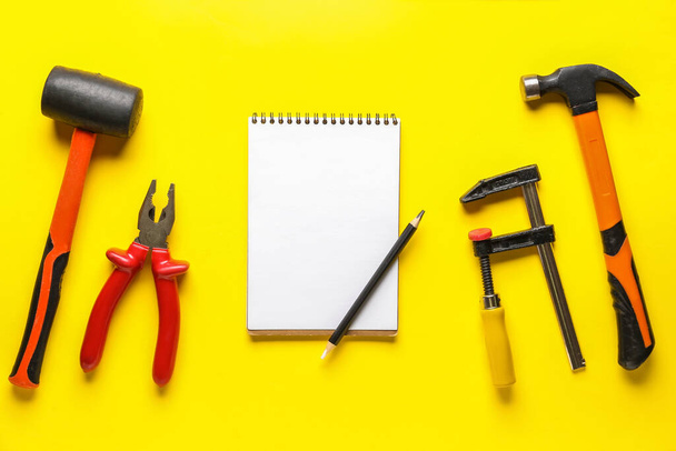 Composição com diferentes ferramentas, caderno e lápis sobre fundo amarelo. Celebração do Dia do Trabalho - Foto, Imagem