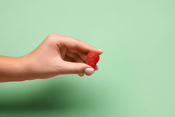 Woman holding fresh raspberry on green background - Photo, Image