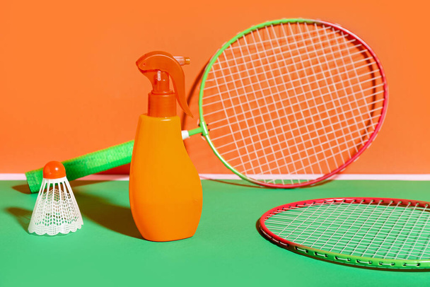 Bottle of sunscreen cream, badminton rackets and shuttlecock on color background - Photo, Image