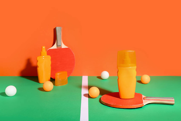 Bottles of sunscreen cream, ping pong rackets and balls on color background - Photo, Image