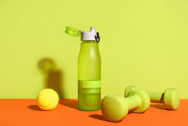 Bottle of water, dumbbells and tennis ball on color background - Photo, image