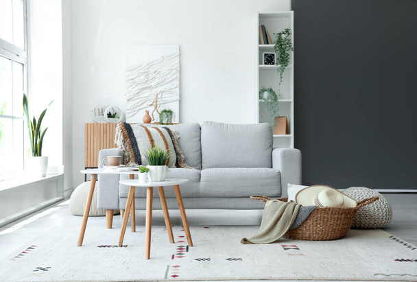 Интерьер светлой гостиной с серым диваном, журнальным столиком и плетеной корзиной - Фото, изображение