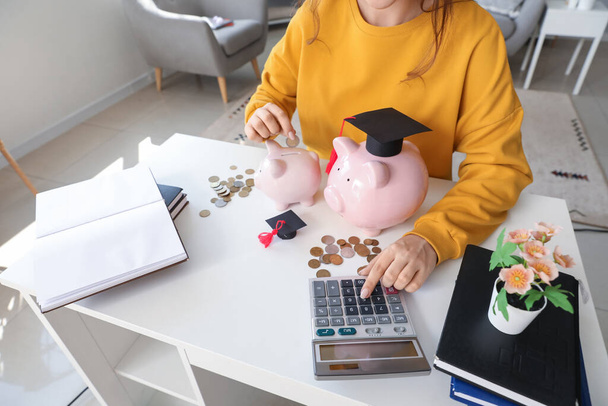 Studentin berechnet Finanzen am Tisch mit Sparschweinen. Konzept für Studienkredite - Foto, Bild