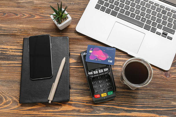 Laptop com terminal de pagamento, xícara de café e cartões de crédito em fundo de madeira marrom - Foto, Imagem