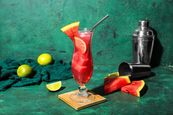 Glass of tasty watermelon cocktail with shakers and lime on grunge green background - Photo, Image