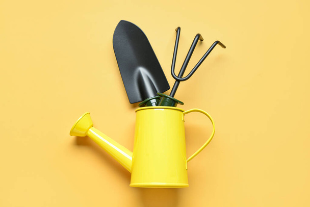 Watering can with gardening rake and shovel on yellow background - Valokuva, kuva