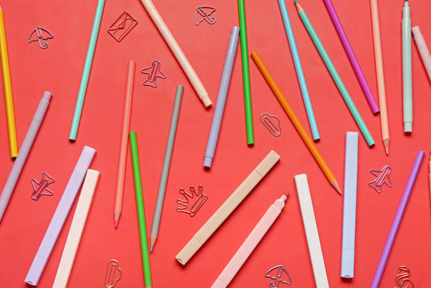 Barevné tužky a značky s kancelářskými sponkami v různých tvarech na červeném pozadí - Fotografie, Obrázek
