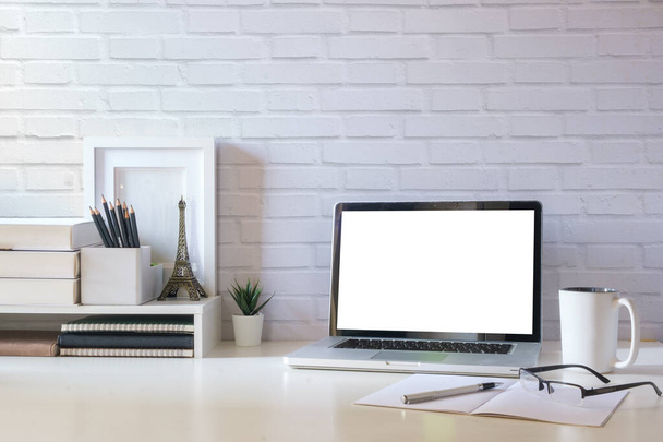 Einfacher Arbeitsplatz mit Laptop, Kaffeetasse, Bilderrahmen und Zimmerpflanze auf weißem Tisch. - Foto, Bild