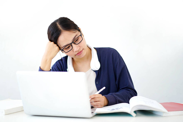 Closeup Asian young female student in casual cloth shows boredom in doing reports or homework with laptop on white gradient background. Asian school concept. - Фото, изображение