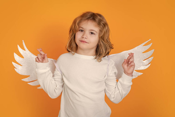 Маленький ангел скрестил пальцы с везунчиком и надеждой, удачи. День Святого Валентина. Маленькое дитя-ангел-купидон с крыльями. Студийный портрет ангельского ребенка - Фото, изображение