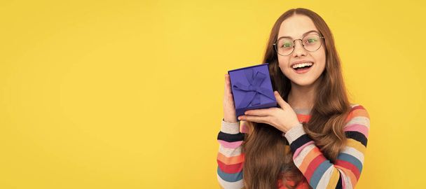 щаслива дівчина-підліток в окулярах тримає подарункову коробку на свято, сюрприз. Маленька дівчинка з подарунком, горизонтальний плакат. Заголовок банера з пробілом для копіювання
 - Фото, зображення