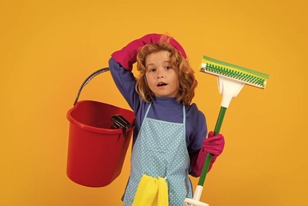 Evde temizlik yapan küçük bir çocuk. Çocuk ev işi yapıyor, eğleniyor. Sarı arka planda ıslak düz paspasla çocuk hizmetçisi portresi - Fotoğraf, Görsel
