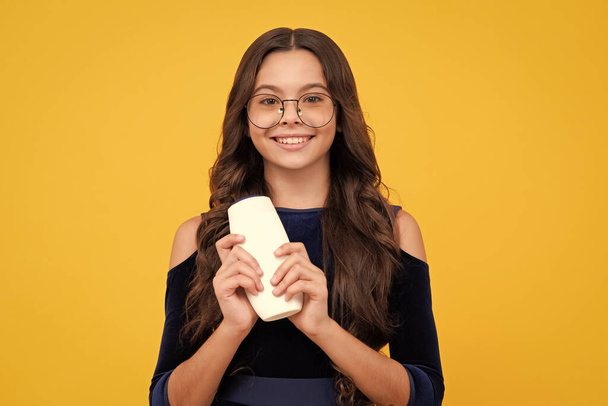 Teenager child girl showing bottle shampoo conditioners or shower gel. Hair cosmetic product. Bottle for advertising mock up copy space. Happy face, positive and smiling emotions of teenager girl - 写真・画像
