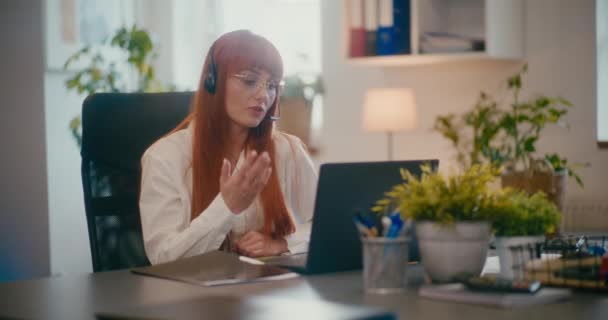 Rood hoofd vrouwelijke klant vertegenwoordiger dragen headset werken op laptop aan bureau in kantoor. - Video