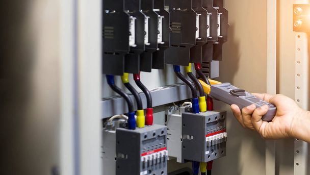 Tester pracy inżyniera elektryka mierzący napięcie i prąd linii elektrycznej w elekcyjnej szafie sterowniczej. - Zdjęcie, obraz