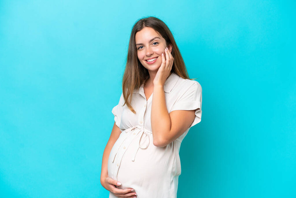 Young caucasian woman isolated on blue background pregnant and happy - Foto, immagini