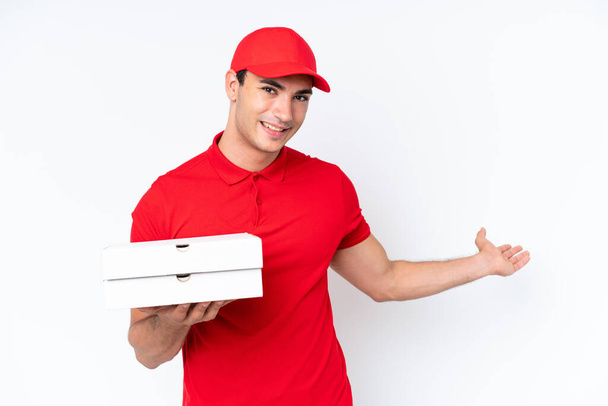 Pizza dodání kavkazský muž s pracovní uniformou vyzvednutí pizza boxy izolované na bílém pozadí natahuje ruce na stranu pro pozvání přijít - Fotografie, Obrázek