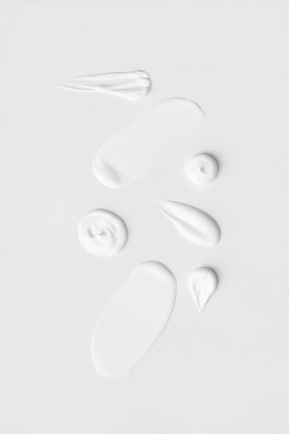 Ένα σύνολο από διαφορετικές πινελιές της λευκής κρέμας σε ένα ελαφρύ φόντο. - Φωτογραφία, εικόνα