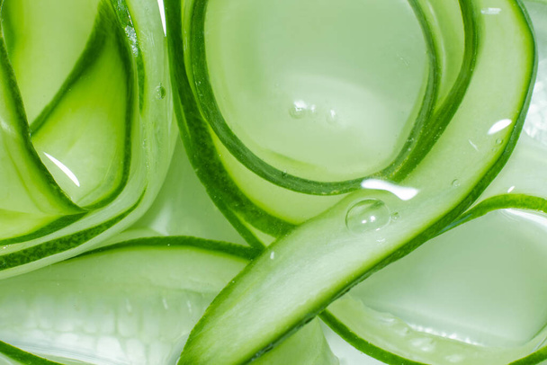 A background of cucumber slices in water. Lots of cucumber slices swirled in water. - Photo, Image