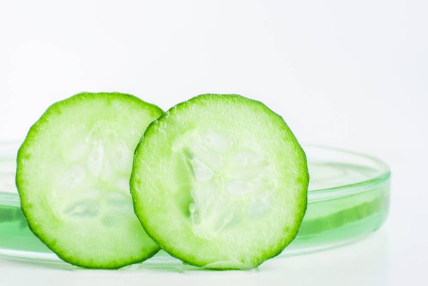 Dunne plakjes verse groene komkommer tegen een petrischaal. - Foto, afbeelding