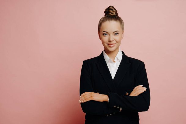 Confident female office worker in formal outfit standing confidently with her arms crossed and looking forward to next opportunities, smiling businesswoman isolated over pink background - Zdjęcie, obraz