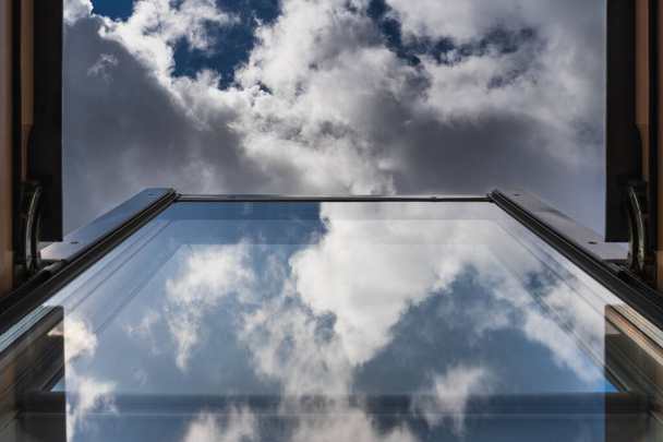 Les cadres du ciel nuageux ouvrent la fenêtre du grenier, avec des nuages éthérés réfléchis dans le verre. L'ambiance Moody capture la beauté de la nature - Photo, image