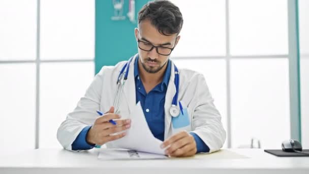 Young hispanic man doctor writing medical report at clinic - Footage, Video