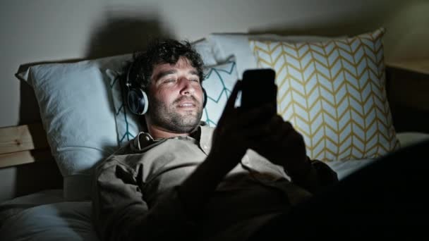 Junger hispanischer Mann hört Musik liegend im Schlafzimmer - Filmmaterial, Video