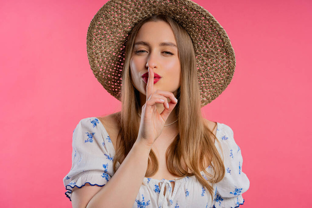 Smiling ukrainian woman holding finger on lips, pink studio background. Pretty lady with gesture of shhh, secret, silence, conspiracy, gossip concept. High quality - Фото, изображение