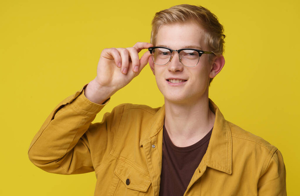 A Young Student looking happy, youth, emotions concept. Cheerful hipster blond young man 20s holding eyewear by hand isolated yellow background. - Photo, image
