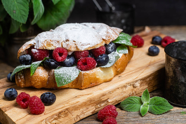 Croissant with raspberries, blueberries and cream cheese on a wooden board - Photo, Image