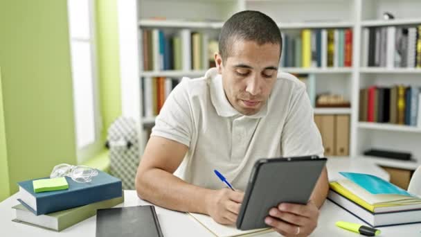 Joven estudiante hispano usando touchpad tomando notas en la universidad de la biblioteca - Metraje, vídeo