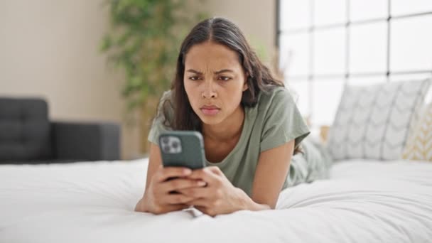 Afrikkalainen amerikkalainen nainen käyttää älypuhelinta makaa sängyllä etsivät järkyttynyt makuuhuoneessa - Materiaali, video