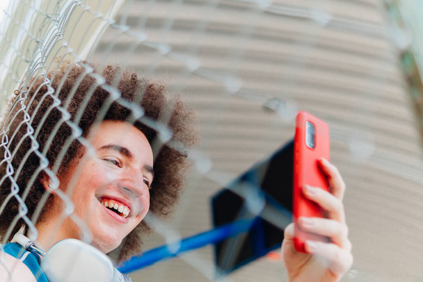 Πορτραίτο με χαμηλή γωνία ενός χαρούμενου αγοριού με ακουστικά και αθλητικά ρούχα που βγάζει selfie - Φωτογραφία, εικόνα
