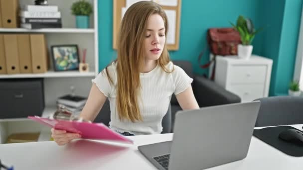 Giovane donna bionda operaia che utilizza il documento di lettura del computer portatile in ufficio - Filmati, video