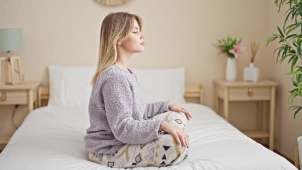 Mujer rubia joven haciendo ejercicio de yoga sentada en la cama en el dormitorio - Metraje, vídeo
