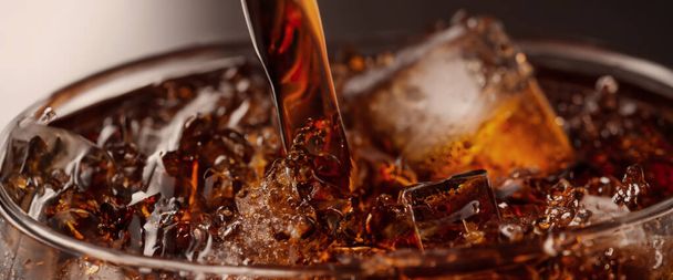 Pouring of Cola and Ice. Cola soda and ice splashing fizzing or floating up to top of surface. Close up of ice in cola water. Texture of carbonate drink with bubbles in glass. Cold drink background - Φωτογραφία, εικόνα
