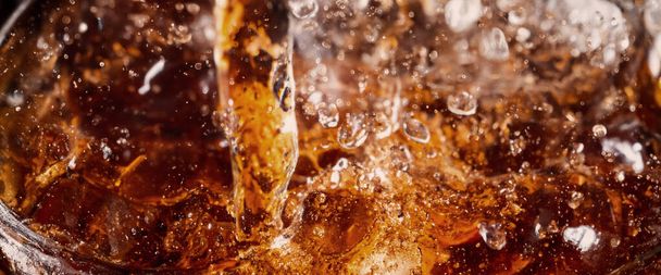 Pouring of Cola and Ice. Cola soda and ice splashing fizzing or floating up to top of surface. Close up of ice in cola water. Texture of carbonate drink with bubbles in glass. Cold drink background - Photo, Image
