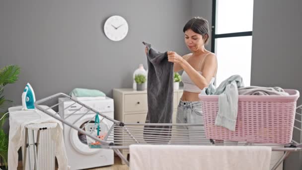 Joven hermosa mujer hispana sonriendo confiado colgando ropa en tendedero en la sala de lavandería - Imágenes, Vídeo