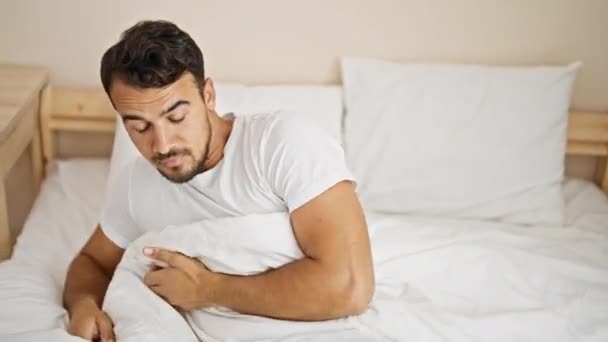Молодой латиноамериканец просыпается с протянутыми руками в спальне - Кадры, видео