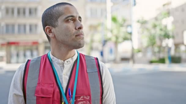 Jonge Spaanse man vrijwilliger draagt vest ziet er serieus uit op straat - Video
