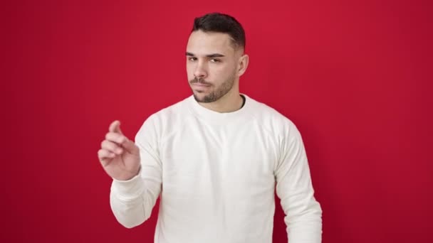 Молодой латиноамериканец говорит нет с пальцем на изолированном красном фоне - Кадры, видео