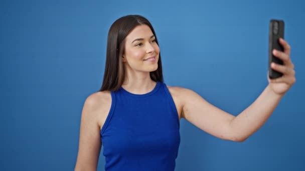 Joven hermosa mujer hispana sonriendo confiada haciendo selfie por el teléfono inteligente sobre fondo azul aislado - Imágenes, Vídeo