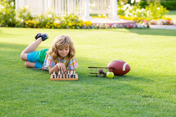 Kid playing chess and having fun outdoor on backyard or summer park. Chess school outdoor. Child think or plan about chess game, laying on grass in summer park. Intelligent and clever school kids - Foto, Bild