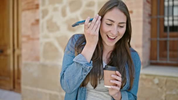 Νεαρή όμορφη ισπανόφωνη γυναίκα ακούει φωνητικό μήνυμα από smartphone πίνοντας καφέ στο δρόμο - Πλάνα, βίντεο