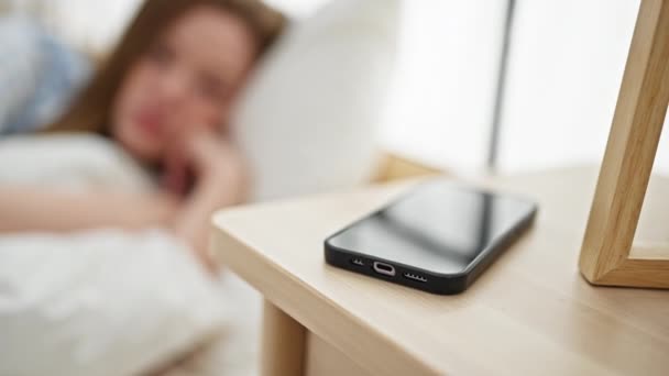 Молода блондинка дивиться смартфон із сумним виразом у спальні - Кадри, відео