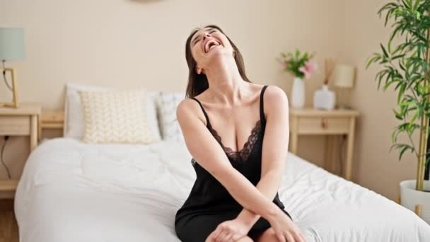 Giovane bella donna ispanica ridendo molto seduto sul letto in camera da letto - Filmati, video