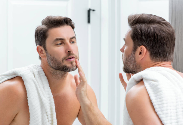 Close-up portrait of perfect brunet man touching chin and skin. Handsome man touching face in front of the mirror in bath. Perfect skin. Man cosmetic, skin treatment. Hygiene and skin care male face - Foto, immagini